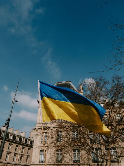 Free Ukrainian national flag on a flagpole against an old city building under a clear blue sky. Stock Photo