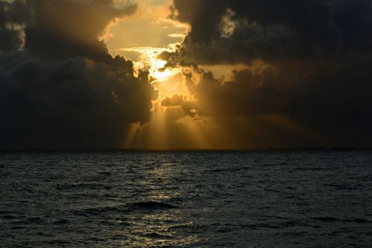 Capture of a dramatic ocean sunset with golden light piercing through clouds over the sea.