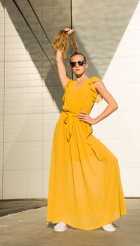 Stylish woman in yellow dress and sunglasses posing confidently against a geometric backdrop.