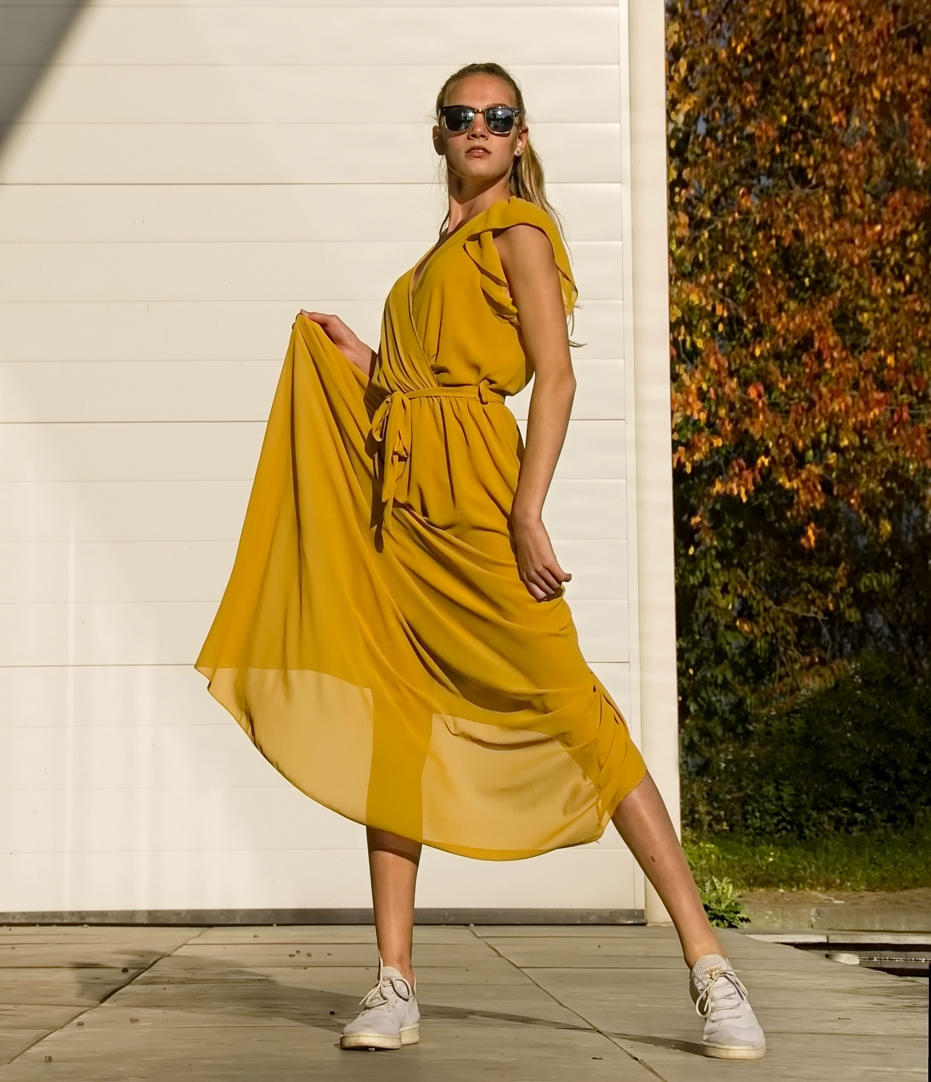 Foto de moda elegante de uma mulher com um vestido amarelo fluido posando ao ar livre sob a luz do sol.