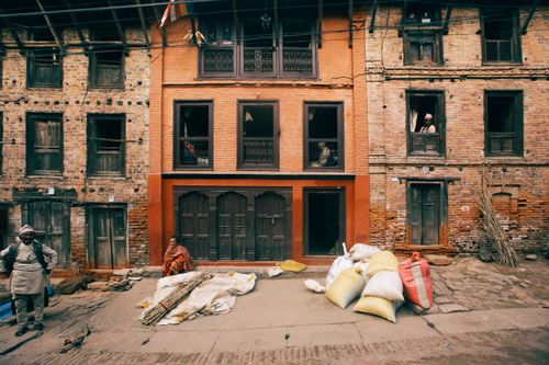 Free A traditional street scene with brick buildings and people handling sacks and sticks, depicting daily life. Stock Photo