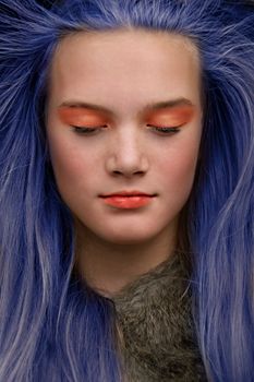 Vibrant portrait of woman with blue hair and orange makeup, eyes closed.