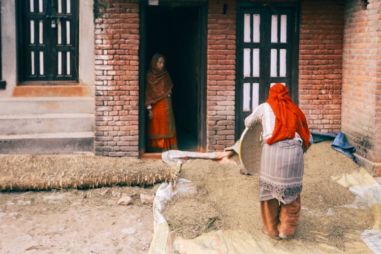 Women Sifting Grain From Chaff In Backyard Of House