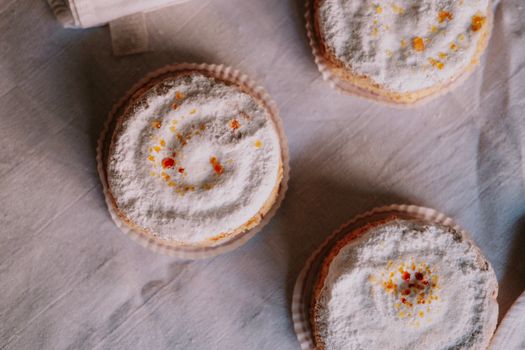 High angle view of three powdered cupcakes with colorful sprinkles on a textured cloth.