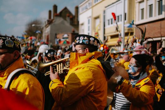 Colorful street festival with musicians in vibrant costumes playing trumpets amidst a lively crowd.