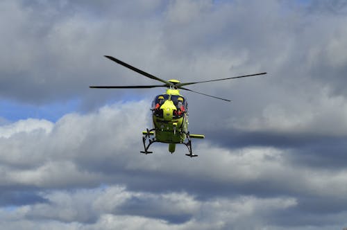 A Green and Black Helicopter Flying Under Dark Clouds