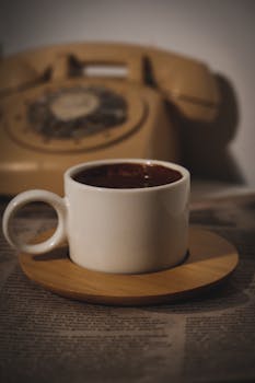 A cozy scene featuring a coffee cup on a saucer next to a vintage rotary phone.