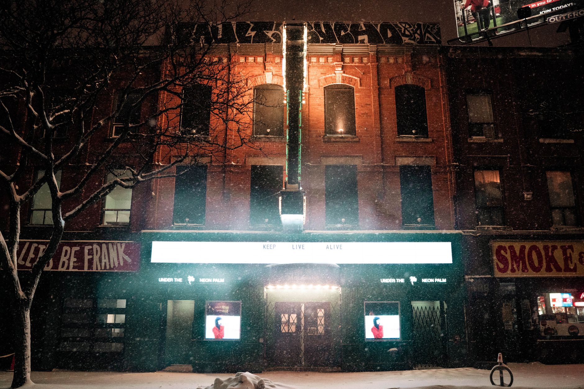 A snowy night captures the vibrant lights of a Toronto street, highlighting urban life and architecture.