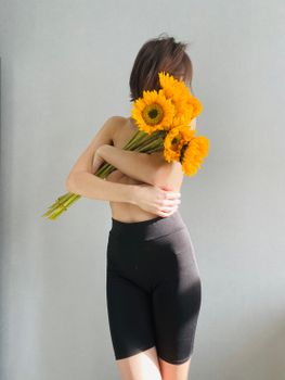 A minimalist portrait of a woman hugging sunflowers, emphasizing elegance and simplicity.