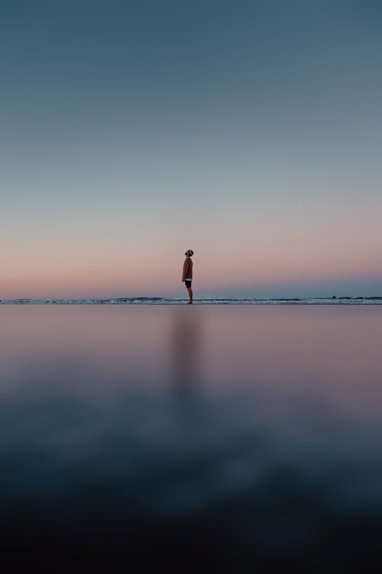 Lonely Man Standing At Seashore And Looking Up In Sky At Dawn