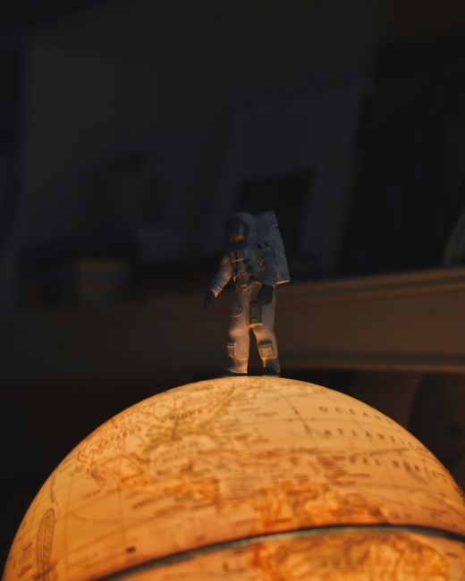 Dramatic shot of a toy astronaut on a glowing globe in a dark room.