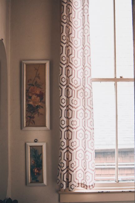 A cozy interior with floral paintings, patterned curtain, and ample natural light through a window. Perfect for living room decor inspiration.