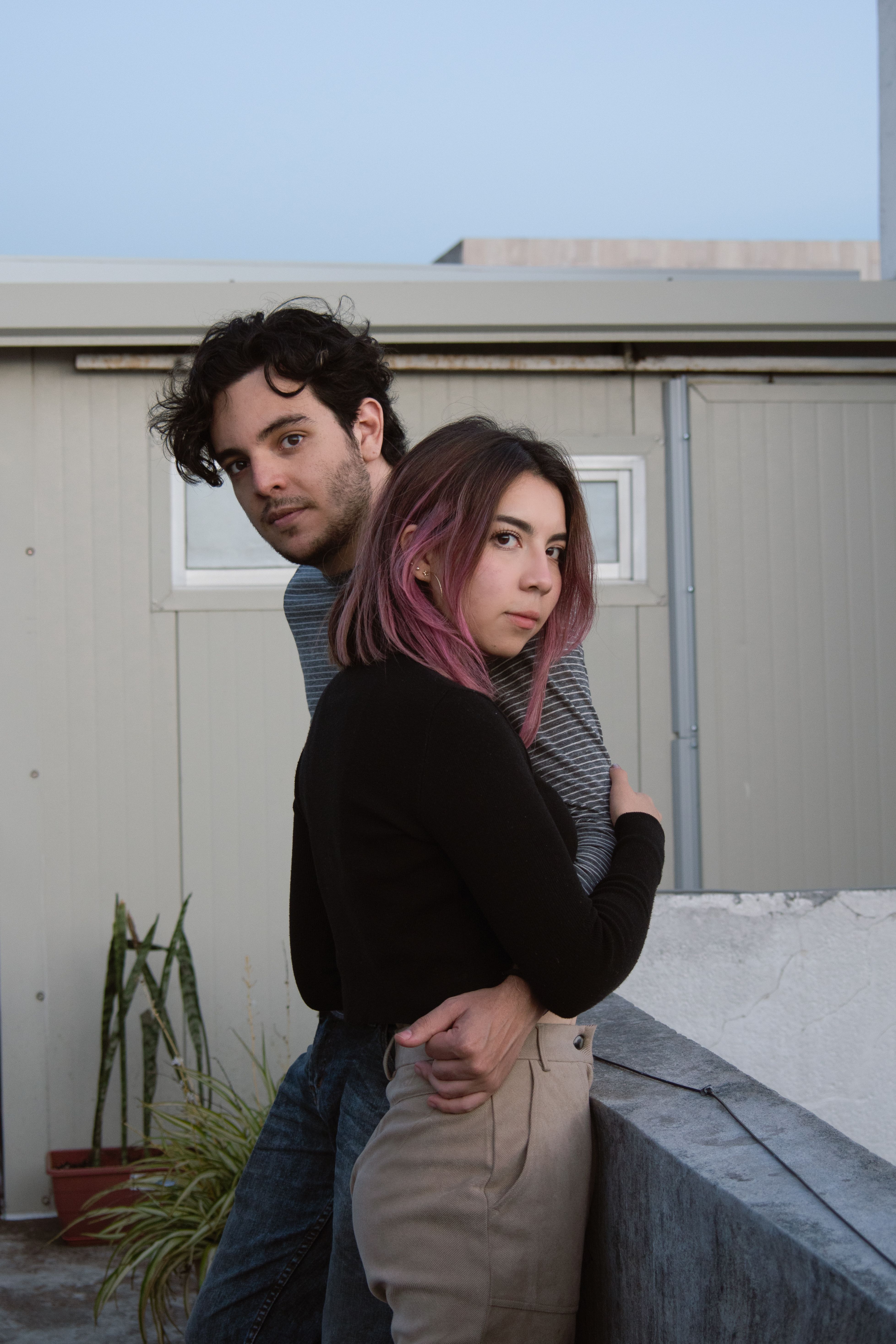Young couple in a casual embrace outdoors by a building, conveying intimacy and style.