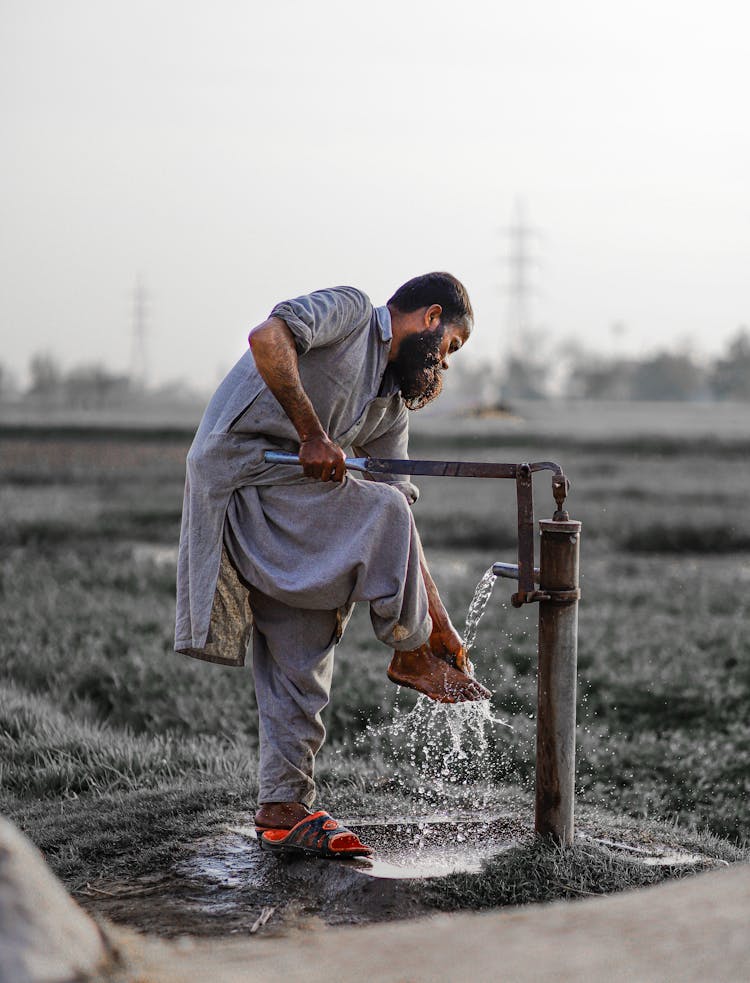 Bearded Adult Man Washing His Foot With Water From Pump 