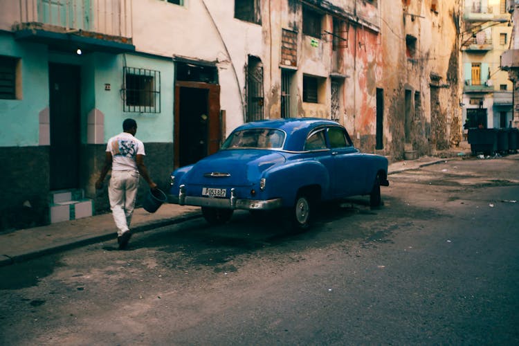 A Man Near A Blue Vintage Car Near Buildings