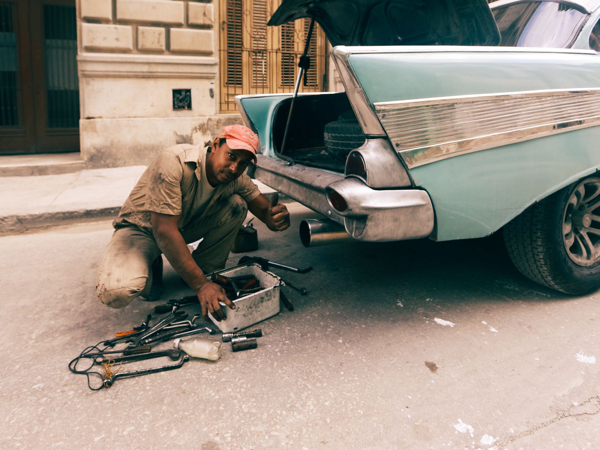 Mechanic gives thumbs up while working on classic car trunk outdoors.