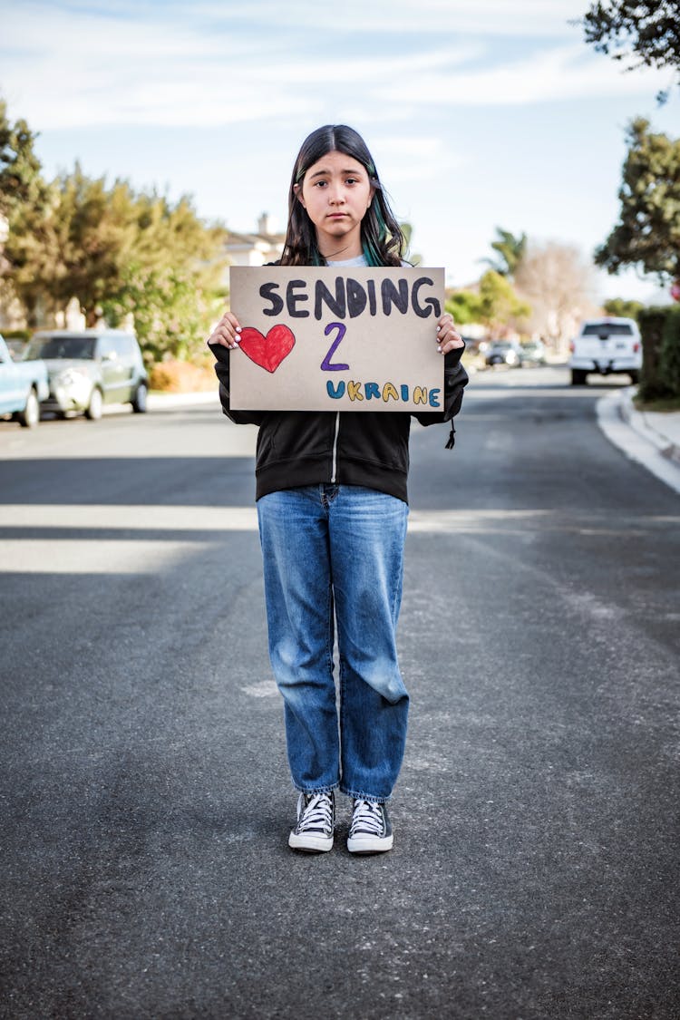 Girl Holding A Placard Standing In The Middle Of A Street