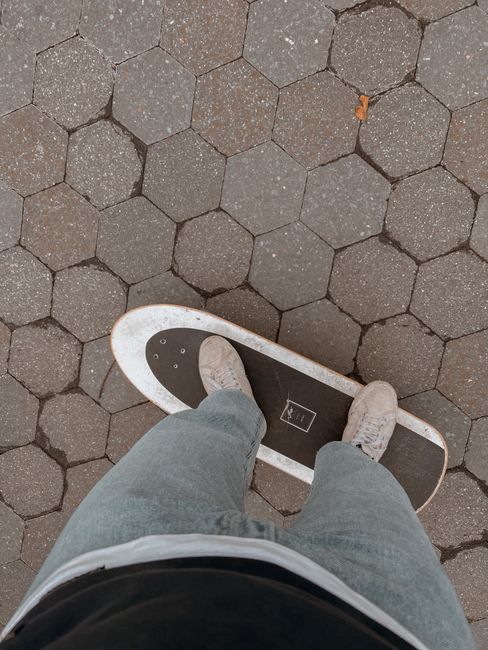 Person standing on skateboard on hexagonal pavement, casual urban scene.