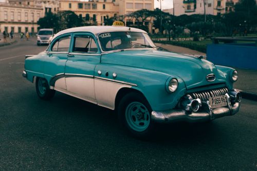 Free A classic turquoise taxi car cruising down an urban street, showcasing retro style. Stock Photo