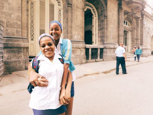 Free Two cheerful friends in school uniforms smiling in front of a historic building facade. Stock Photo