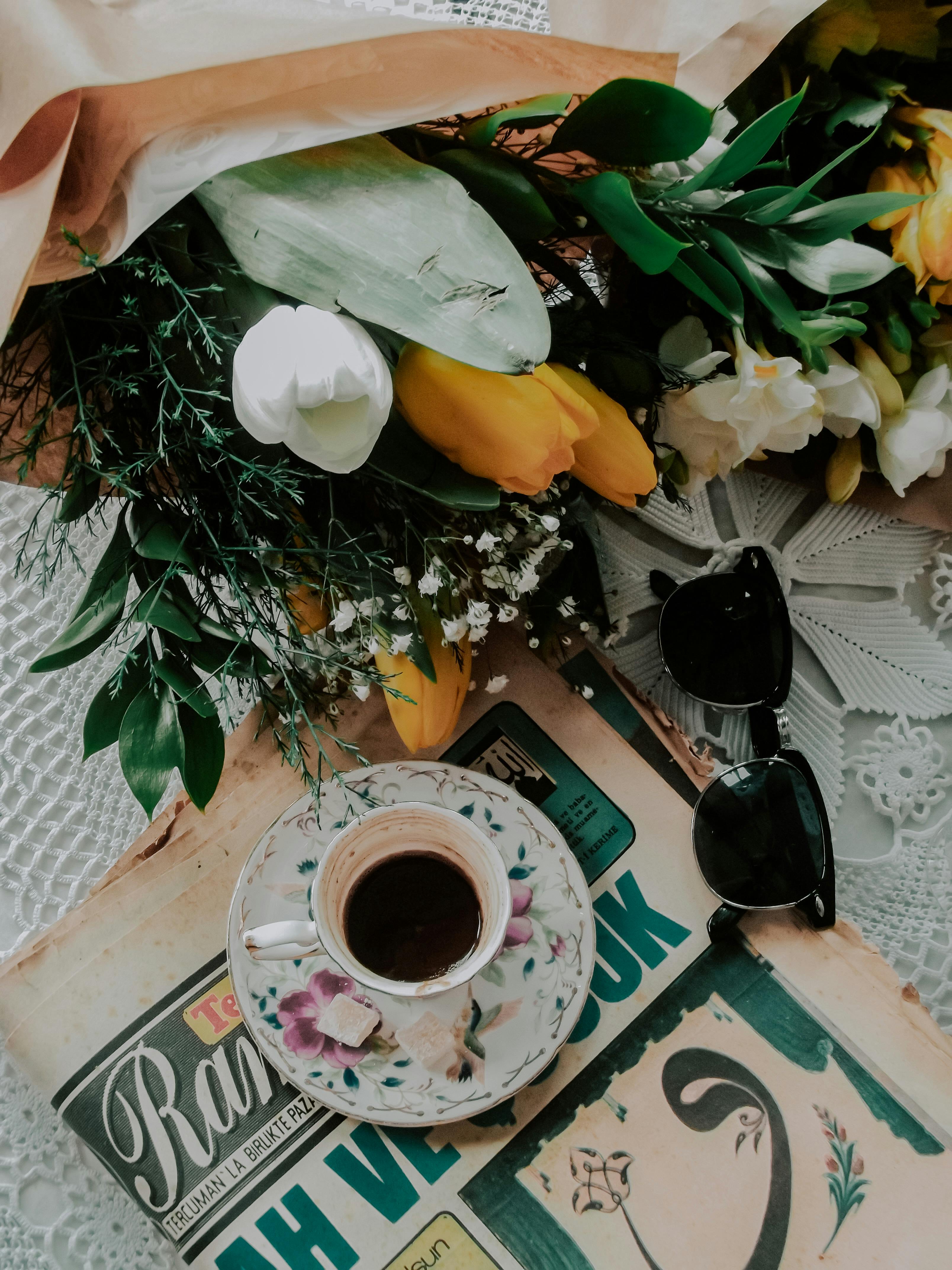 A charming scene with fresh tulips, coffee cup, sunglasses, and a magazine on a lace tablecloth.