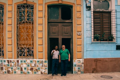 Men Wearing a Grey and Green Shirt Standing Infront of a Orange and Blue Building