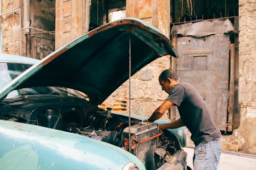 A Man in Gray T-shirt and Denim Pants Fixing a Car