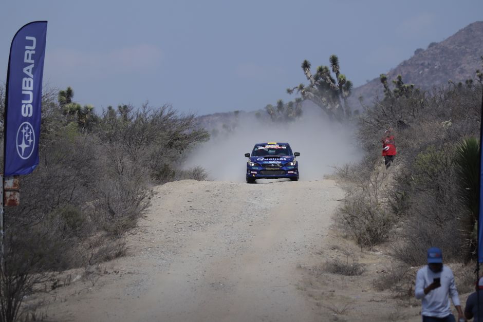 Exciting rally car race on a dusty desert road with Subaru vehicle speeding by.