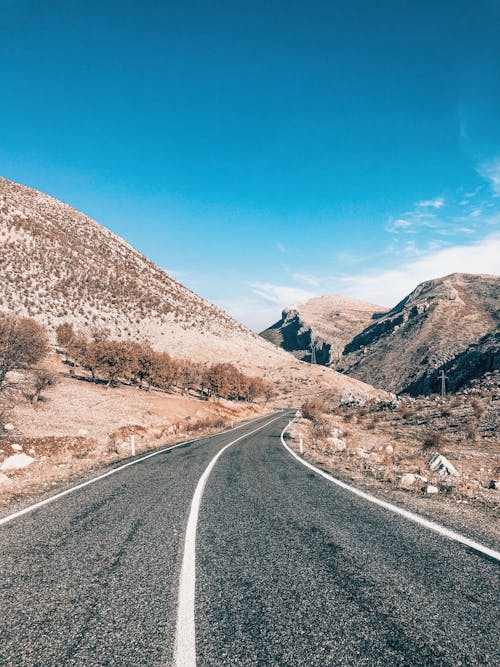 A Gray Concrete Road Near Brown Mountain Under Blue Sky