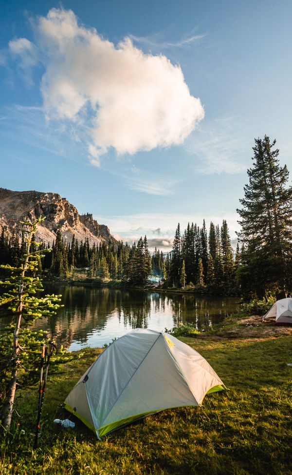 White tent on grass beside a still mountain lake fringed with pine trees