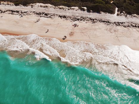 A picturesque aerial shot of a sandy beach with turquoise waves meeting the shore on a sunny day.