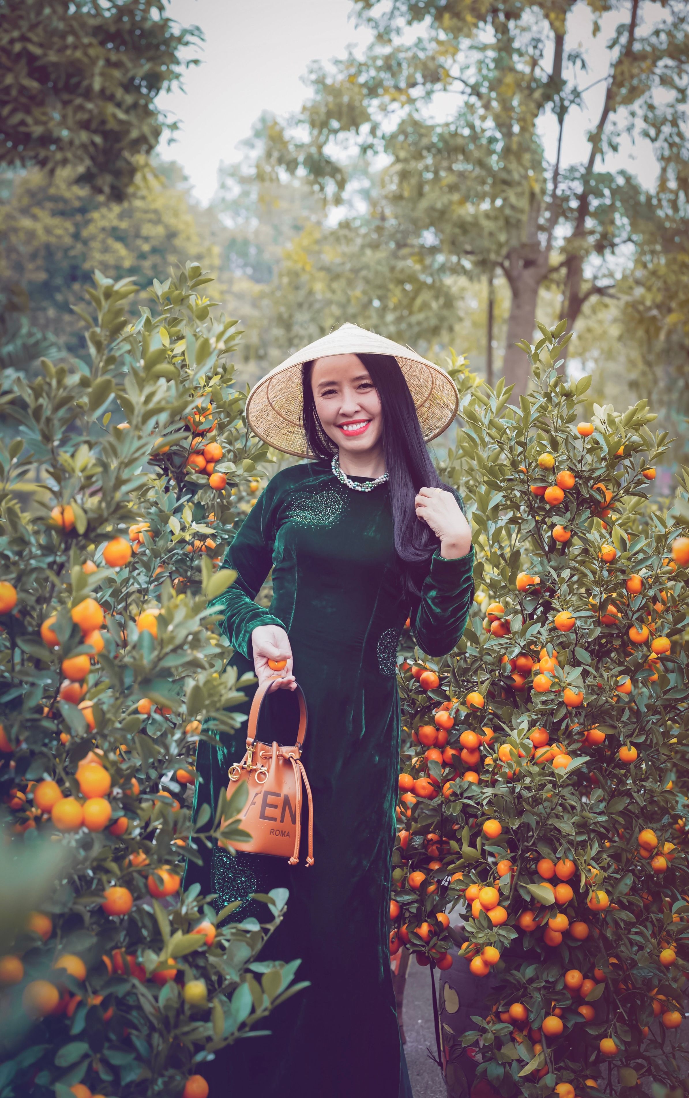 Smiling woman in traditional dress and hat standing among vibrant orange trees, exuding happiness.