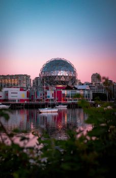 Beautiful reflection of Vancouver's Science World on calm evening waters with pink sunset sky.