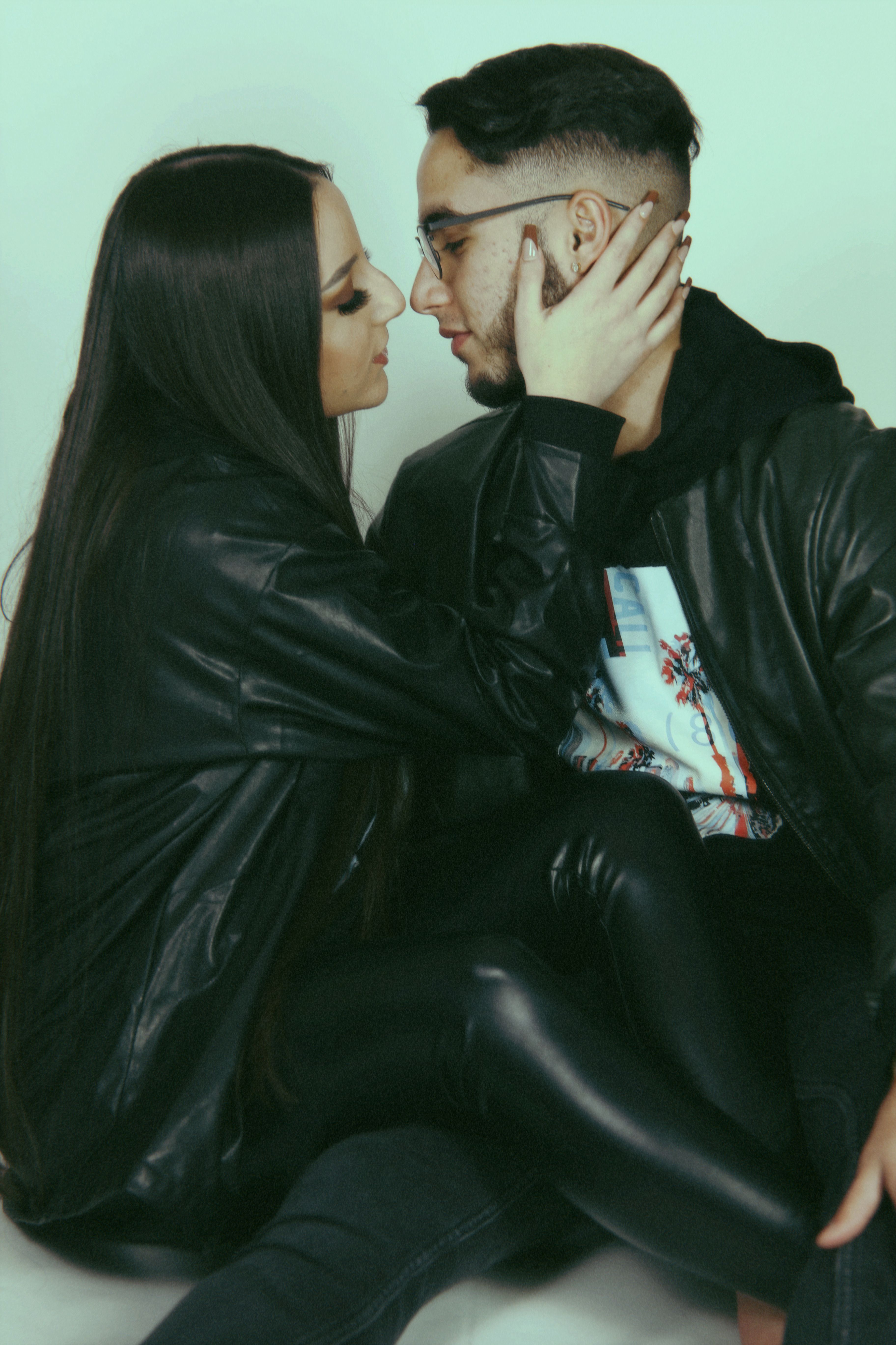 Stylish young couple wearing leather in a tender embrace, captured in a studio setting.