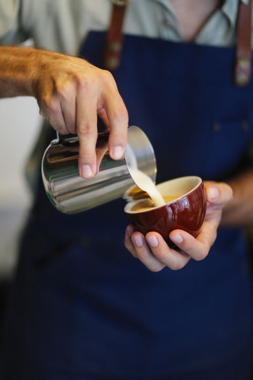 Free Close-up of a barista expertly pouring milk into a coffee cup, showcasing latte art technique. Stock Photo