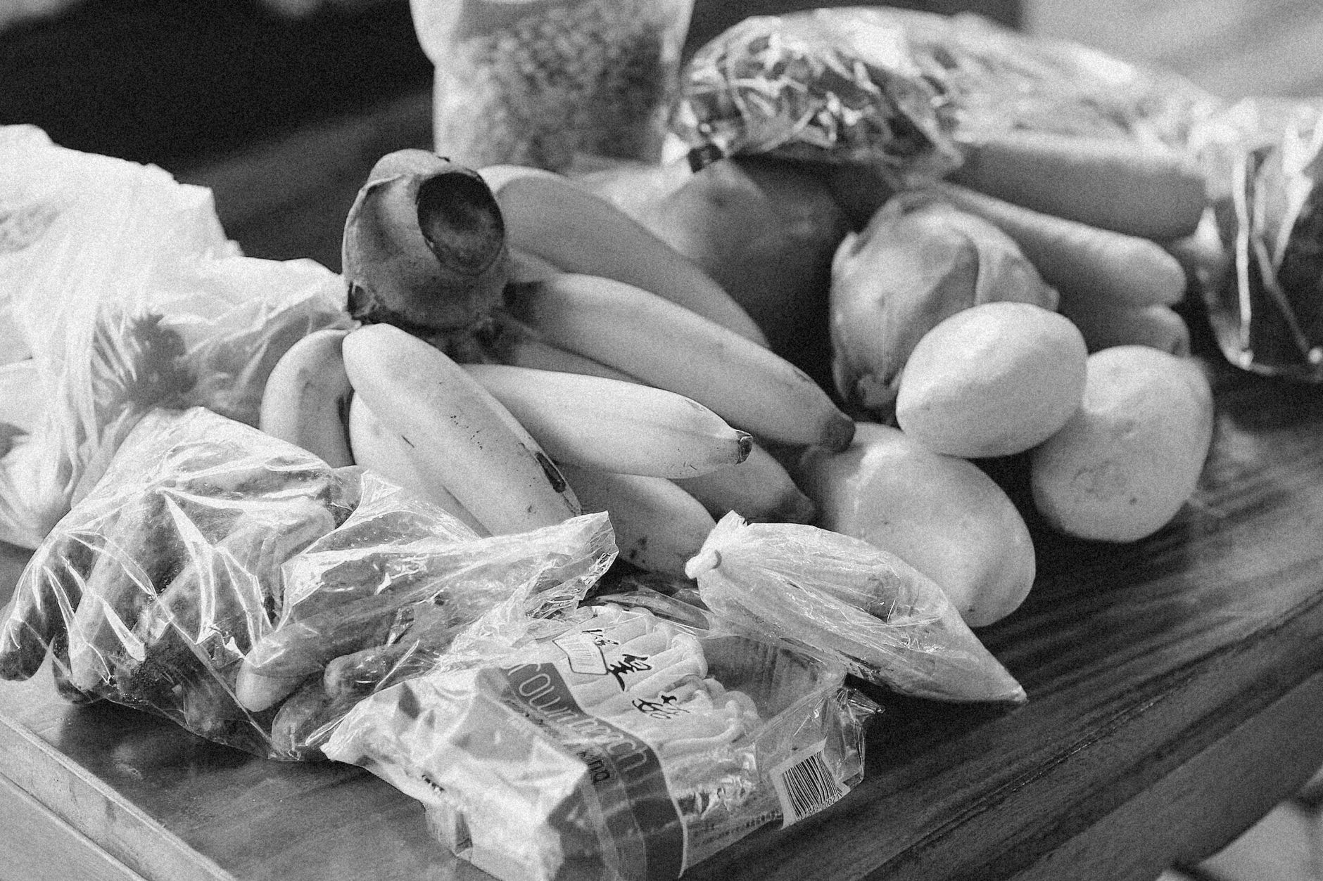 Monochrome close-up of assorted fruits and vegetables in bags on a table.