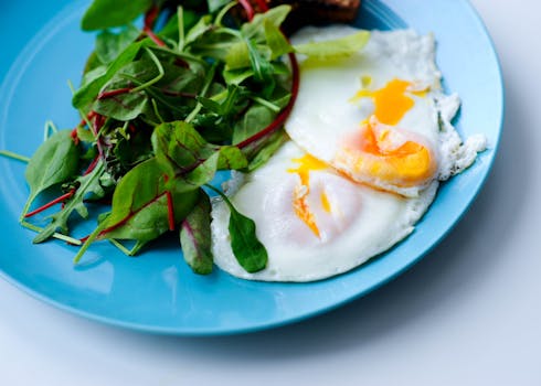 A close-up of a nutritious breakfast with fried eggs and salad greens on a blue plate.