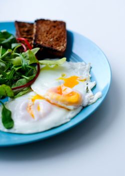 A nutritious breakfast featuring fried eggs, salad greens, and toast on a blue plate.