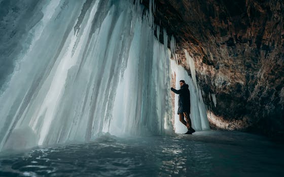 A man stands inside a stunning ice cave adorned with large icicles, exploring its natural beauty.