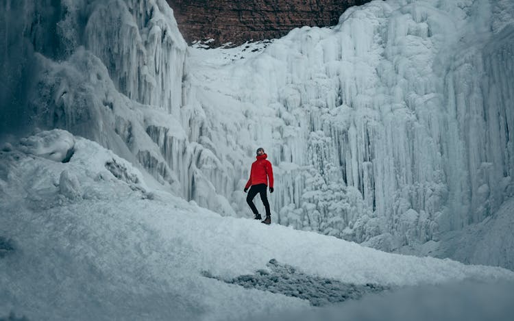 Person In Red Jacket And Black Pants Standing On Snow Covered Ground