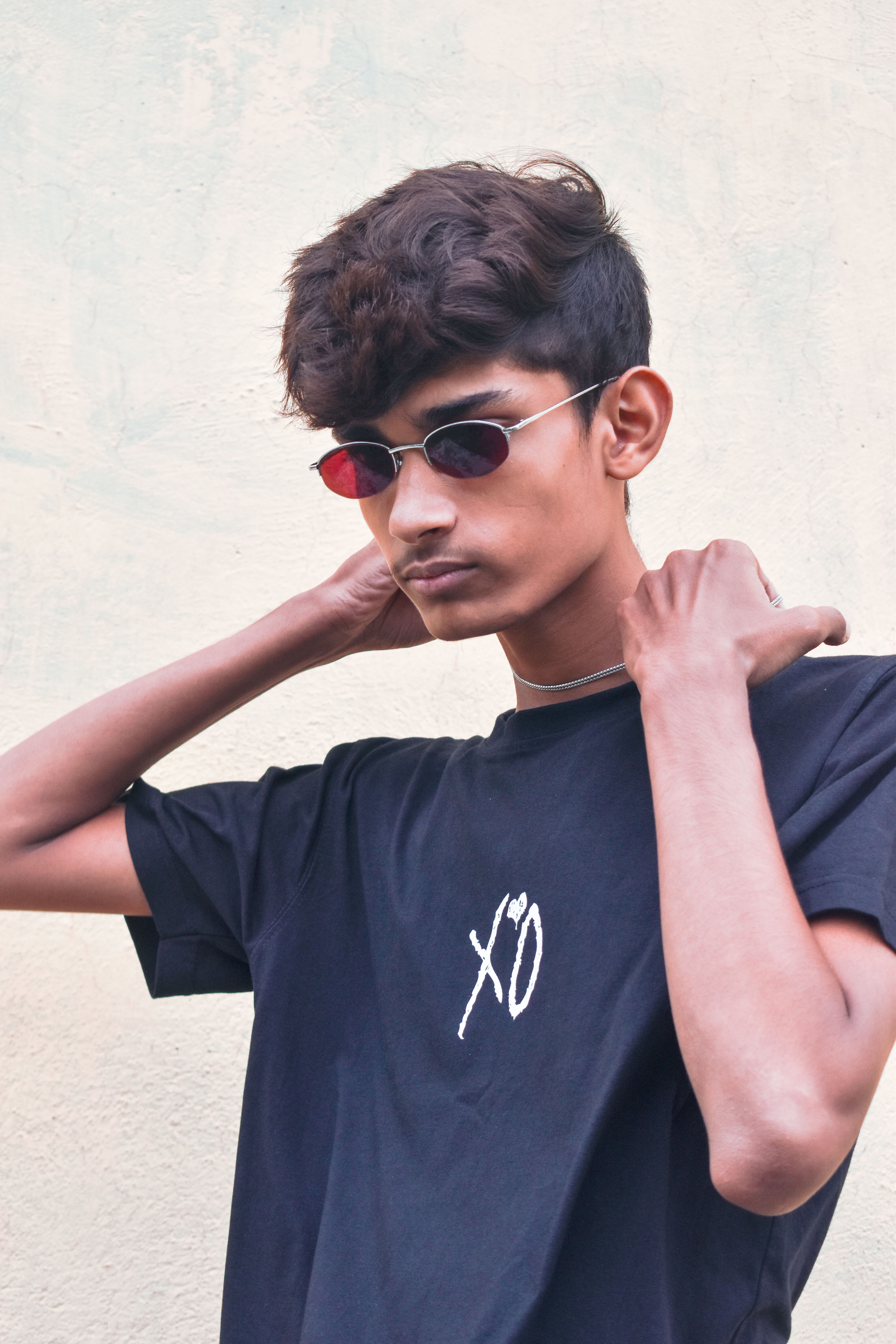 Portrait of a stylish young man wearing sunglasses and a black XO shirt outdoors.
