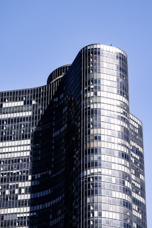 Free A striking modern glass skyscraper with unique architecture against a clear blue sky in downtown Chicago. Stock Photo