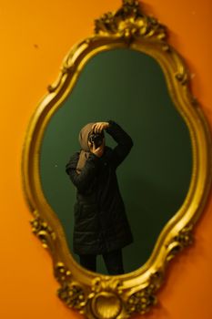 Woman in headscarf taking a photo reflected in an ornate vintage mirror.