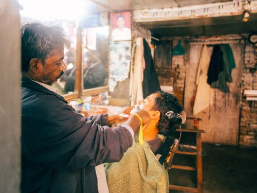 Free Man receives traditional shave in rustic barber shop setting, focusing on personalized grooming. Stock Photo