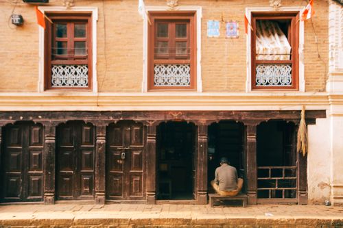 Free Rustic urban facade with open doorways and a seated individual, capturing architectural charm. Stock Photo