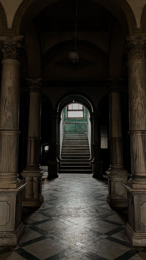Free Dimly lit corridor with grand columns and staircase, exuding vintage charm and architectural elegance. Stock Photo