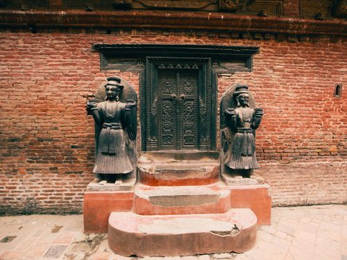 Free A detailed view of a temple entrance with ornate door and carved statues flanking brick walls. Stock Photo