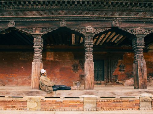 Free Man relaxing against a historic temple with intricate wood carvings in Kathmandu, Nepal. Stock Photo
