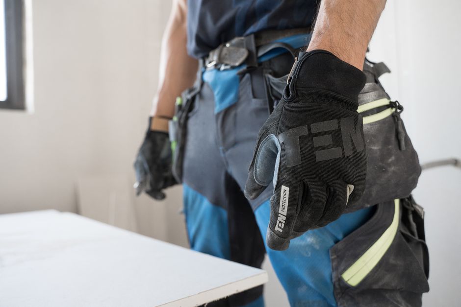 Close-up of a construction worker wearing safety gloves indoors, focused on hand protection.