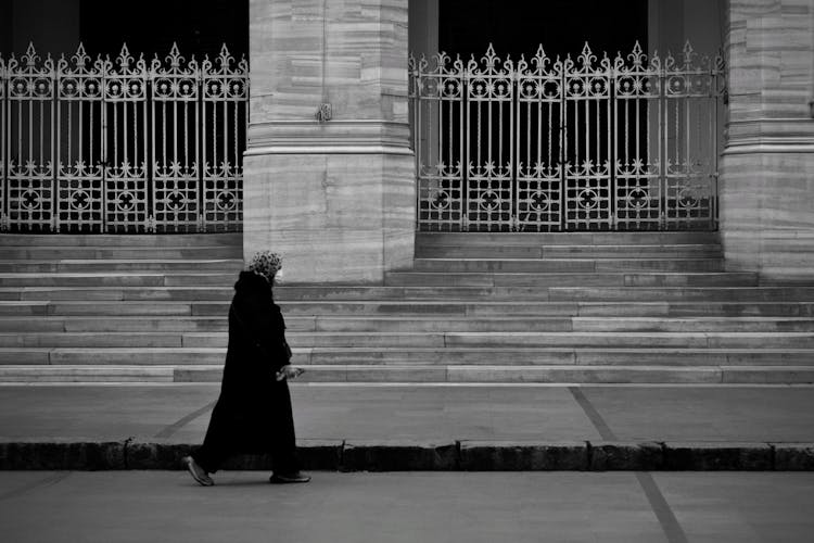 Grayscale Photo Of A Person In A Robe Walking On The Street